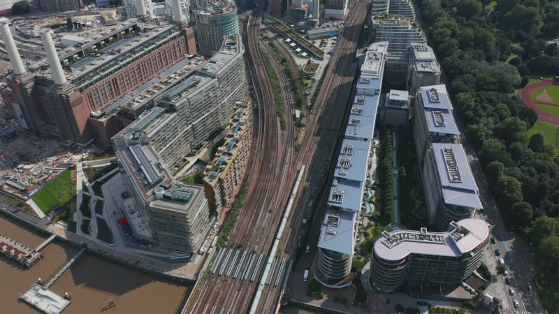 High angle view of train driving on multi track railway line leading between apartment houses at Battersea Power Station. Tilt up reveal cityscape. London, UK