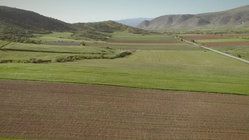 Aerial view of grass fields surrounded by vegetation and hills.