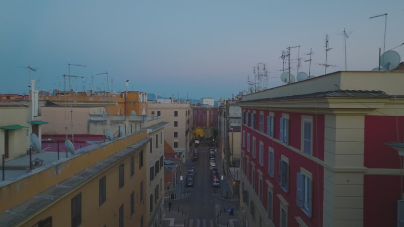 Vorwärts fliegen Sie über eine Straße, die von mehrstöckigen Mehrfamilienhäusern mit farbigen Fassaden gesäumt ist. Stadtbezirk in der Abenddämmerung. Rom, Italien