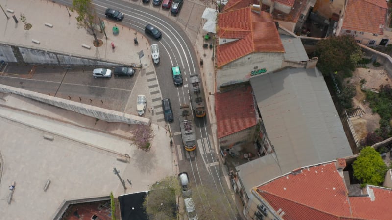 Two tram cars passing by each other in narrow town street. Aerial view from drone. Lisbon, capital of Portugal.