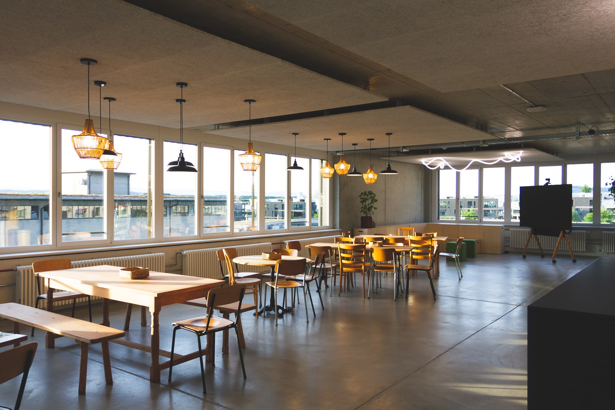 The picture shows seating, similar to a canteen. In front of it is a row of windows; a building roof can be recognised through the windows.