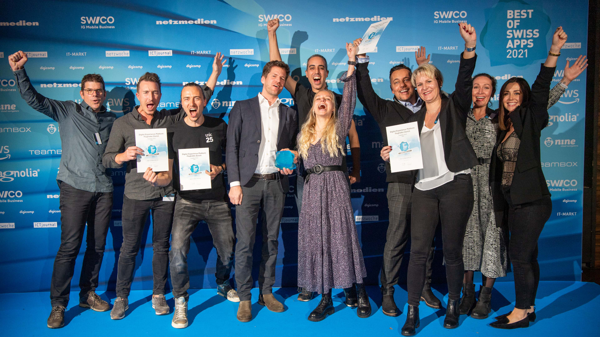 Das Bild zeigt das Unic Gewinner-Team des Projektes Flughafen Zürich. Das Team steht fürs Foto zusammen und die Damen und Herren reißen vor Freude die Arme hoch.