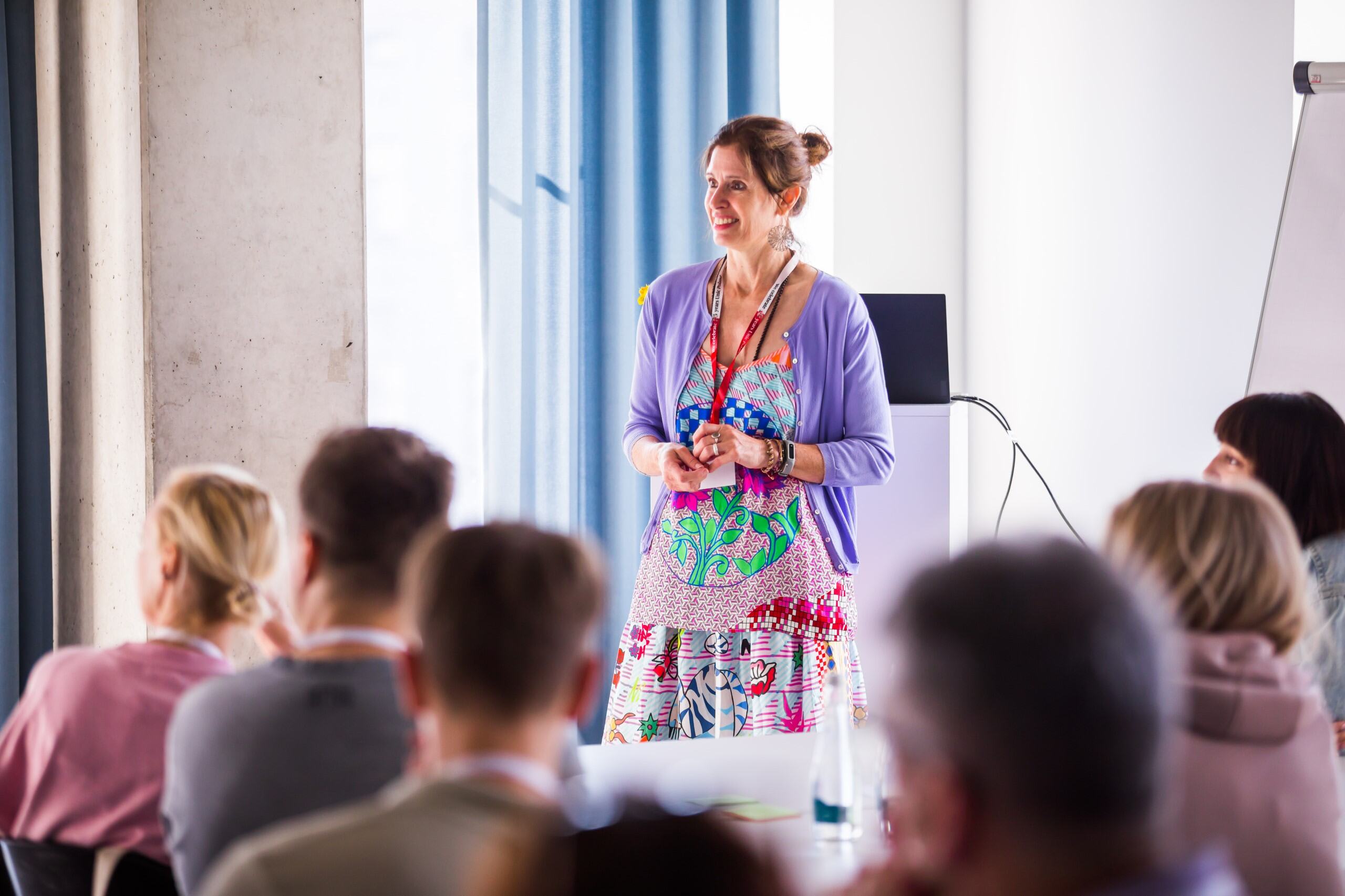 Unic project manager Melanie Klühe stands in front of her audience as a speaker. She is wearing a colourful dress and a purple cardigan.