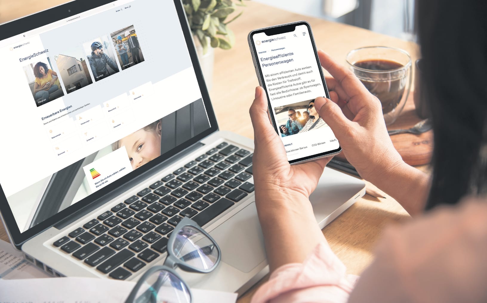 The picture shows a notebook with the SwissEnergy website. A woman is sitting in front of the device while researching efficient mobility on her smartphone.