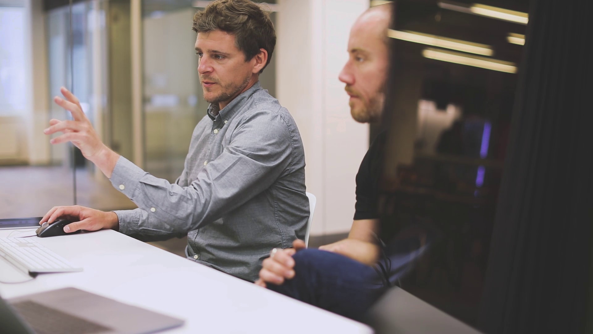 The picture shows two men looking intently at a screen. You can't see the screen, but you can see that one of the men is working with the mouse and gesticulating with his left hand.