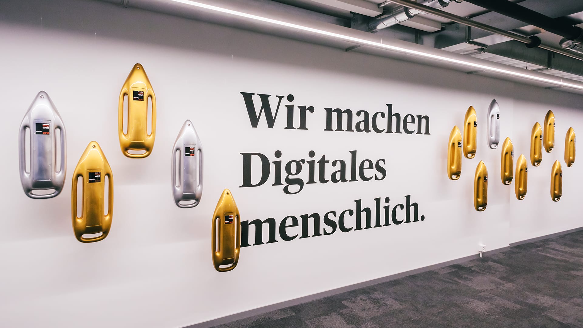 Das Bild zeigt eine Unic Wand mit den vielen Gewinner-Trophäen: silberne und goldene Bojen. In der Mitte des Bildes, bzw. der Wand, erkennt man den Schriftzug Wir machen digitales menschlich.