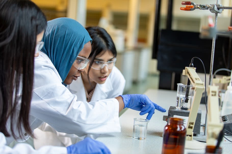 Science students gather closely around an experiment.