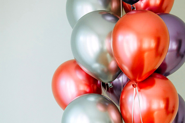 Bunte Luftballons in Silber, Rot und Violett gruppiert für DIY-Geburtstagsgeschenke, vor grauem Hintergrund.
