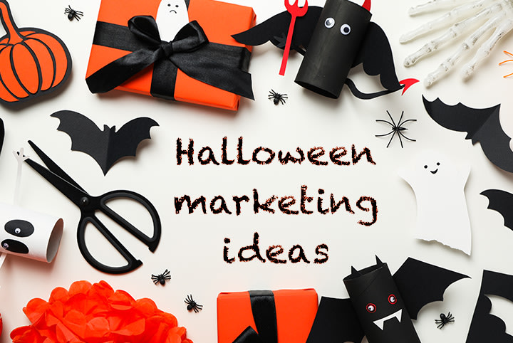 Helovino dekoracija su rankų darbo šikšnosparniais ir oranžinėmis dovanų dėžutėmis su juodu kaspinu – tekstas „Halloween Marketing Ideas“ kūrybinėms kampanijoms.
