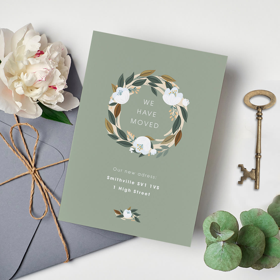 Anledningsflis med bevegelig tema: Elegant flyttekort med en blomsterkrans og teksten "We Have Moved" på grå bakgrunn, ved siden av en nøkkel, konvolutt, hvit blomst og grønt blad.