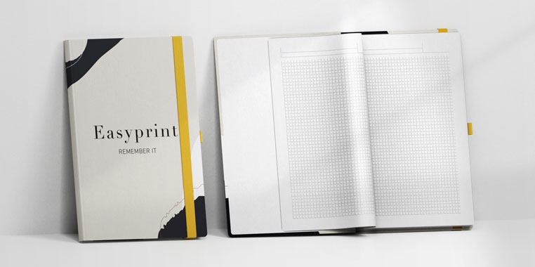 Zwei Notizbücher: Eines geschlossen mit modernem Design, Gummiband und der Aufschrift "Remember it", das andere offen mit karierten Seiten, ideal zum Schreiben.