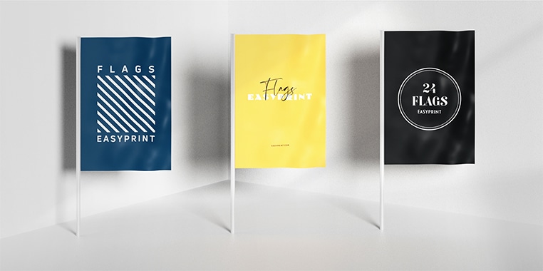 Drei farbige Fahnen in blau, gelb und schwarz-weiß mit Aufdrucken, auf weißen Fahnenstangen vor hellem Hintergrund.