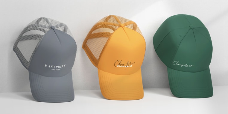 Drei Basecaps in Grau, Gelb und Grün, jeweils mit stilvollen, weißen Schriftzügen auf der Stirnseite, präsentiert vor einem schlichten Hintergrund.