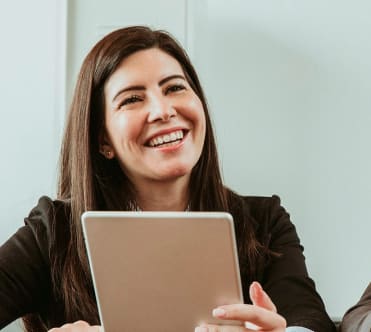 A woman smiles as she looks at a portable device during an office meeting. 