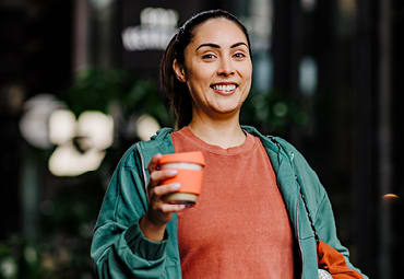 A woman smiles as she holds a reusable takeaway coffee cup.