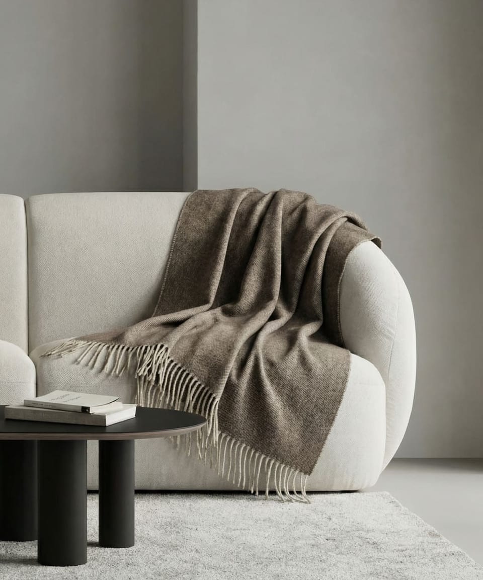 Olive-taupe yak wool throw with tassels draped over a cream sofa in a modern interior