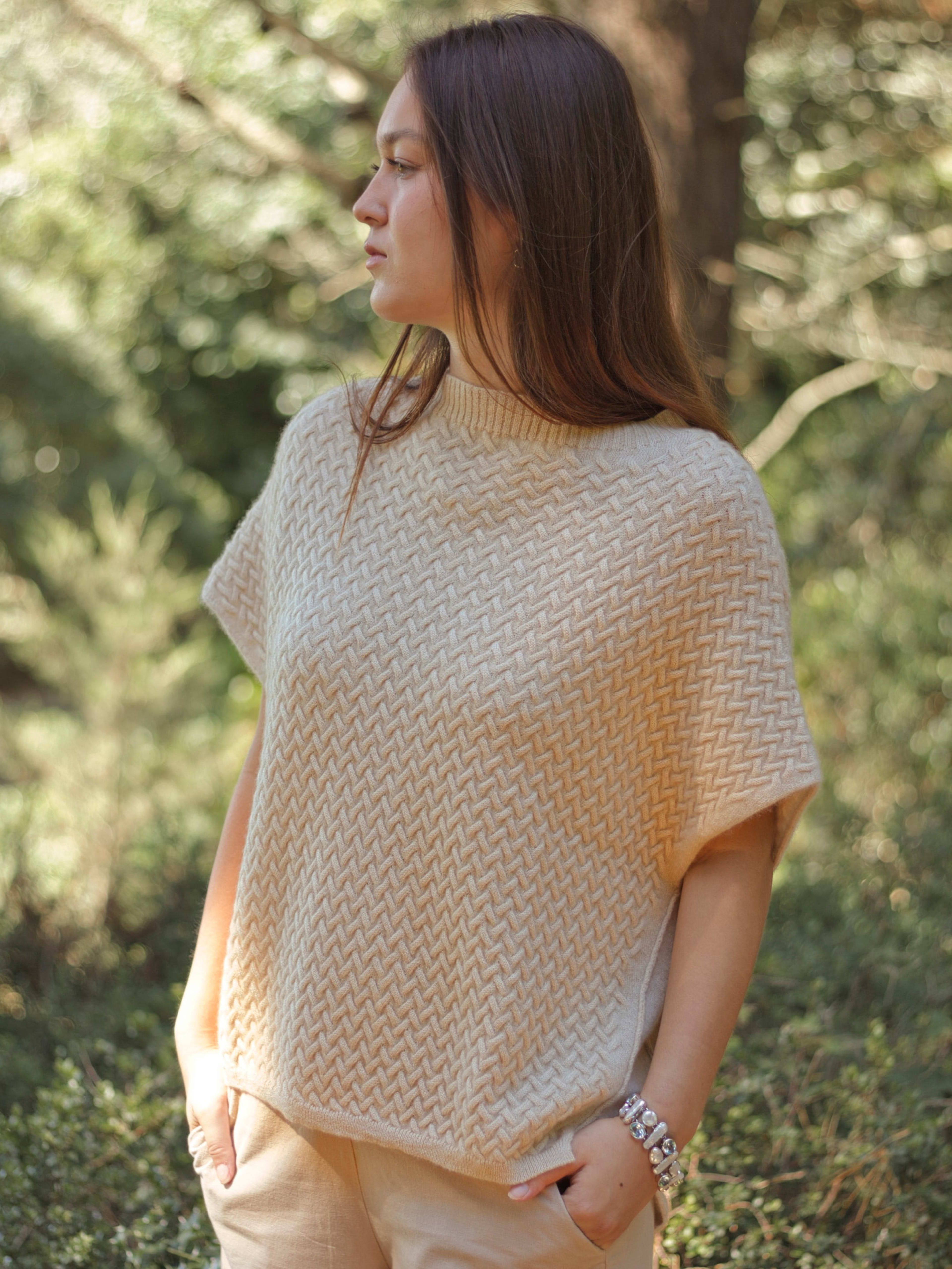 Model outdoors wearing a natural beige luxury cable knit cashmere vest, front view