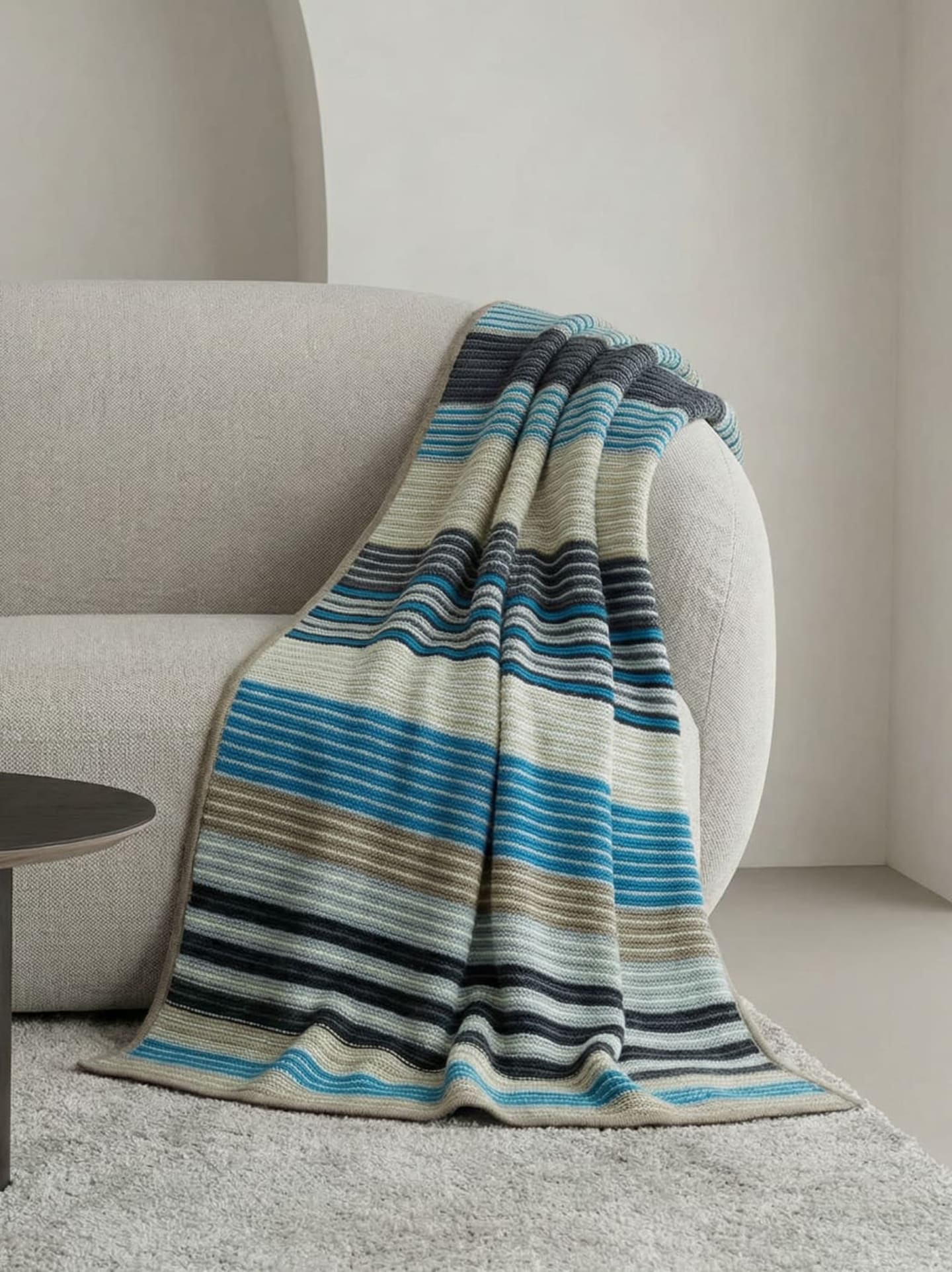 Multi-coloured striped heavyweight cashmere throw in blue, navy, cream and taupe with taupe bound edge, draped over a pale linen round-backed sofa