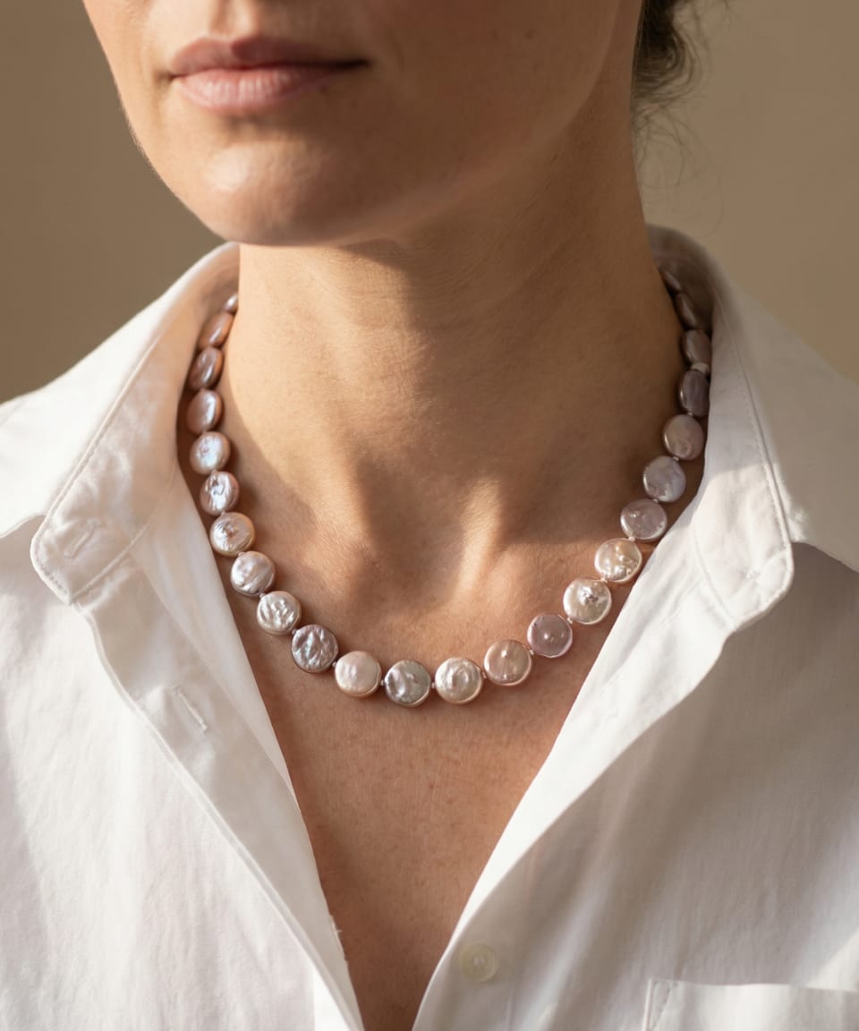 Woman wearing a knotted multi-colour button pearl strand necklace at the collarbone over a white shirt, natural peach and lavender pearl tones
