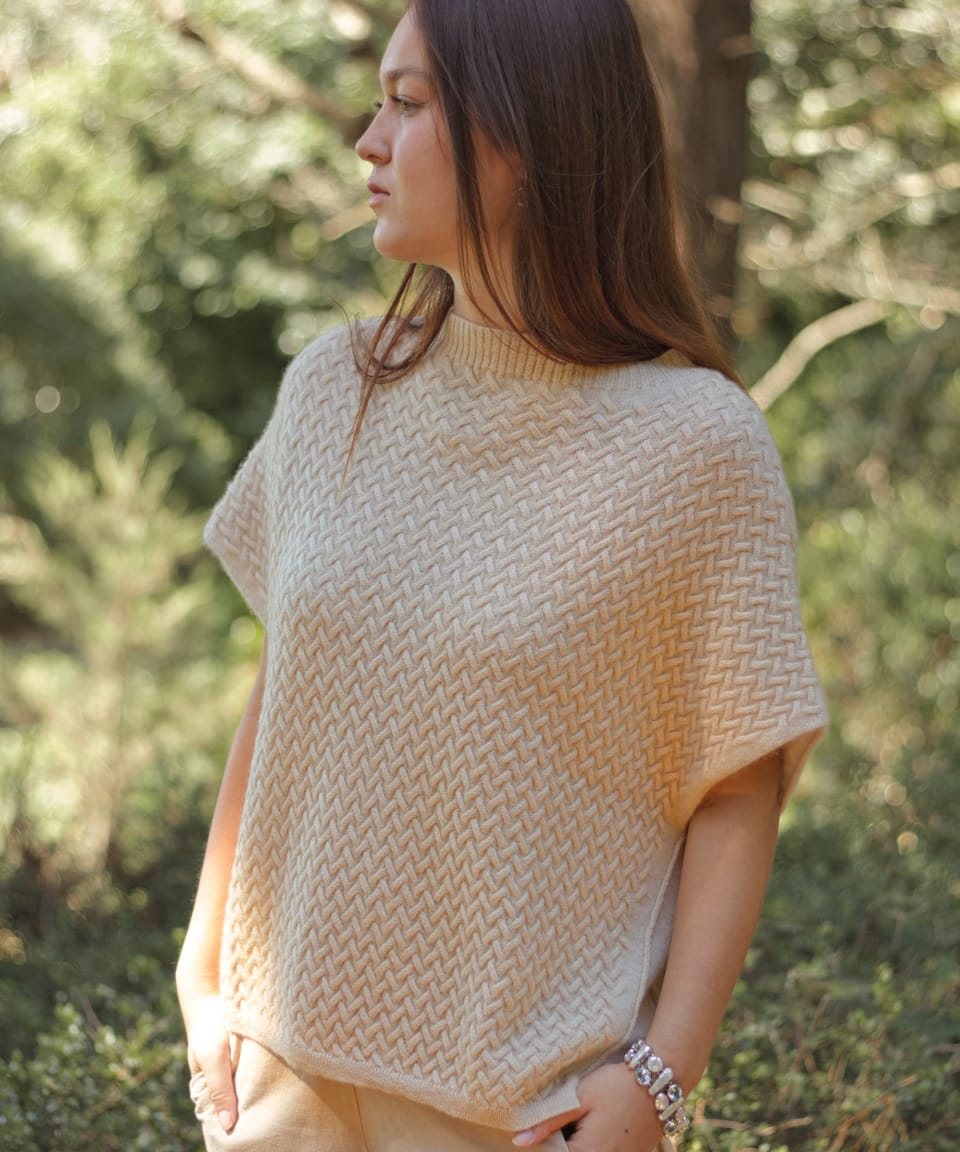 Model outdoors wearing a natural beige luxury cable knit cashmere vest, front view