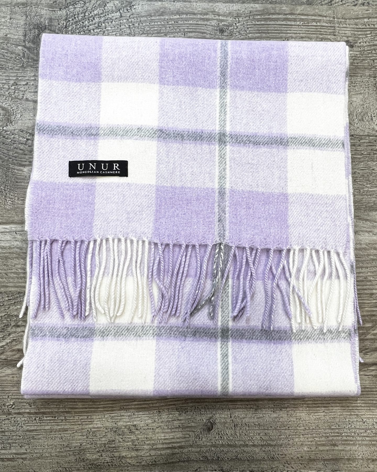 Lay flat of a unisex woven cashmere scarf in tartan purple with tasselled fringe