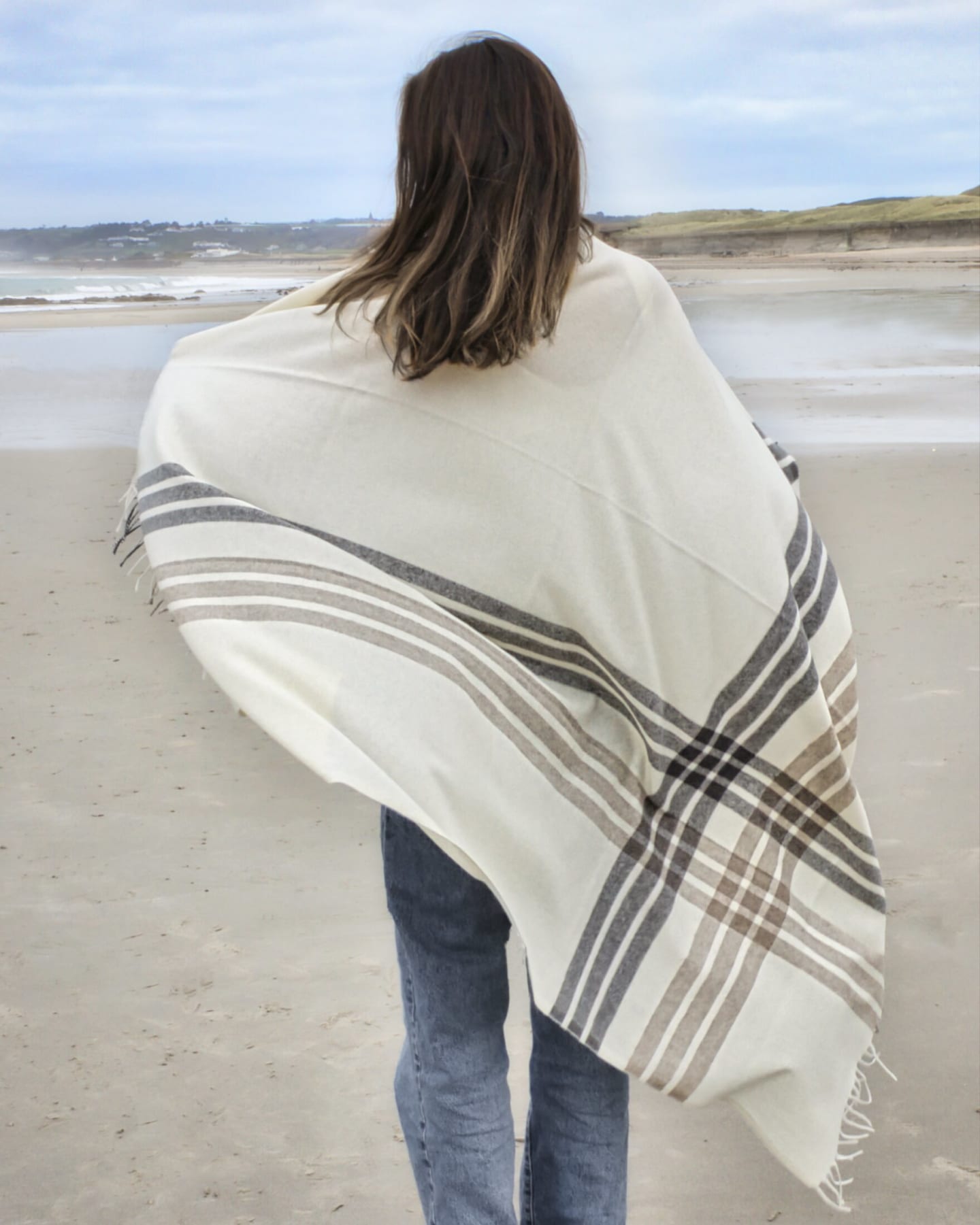 Woman on beach wrapped in a natural white plaid cashmere wrap shawl, rear view