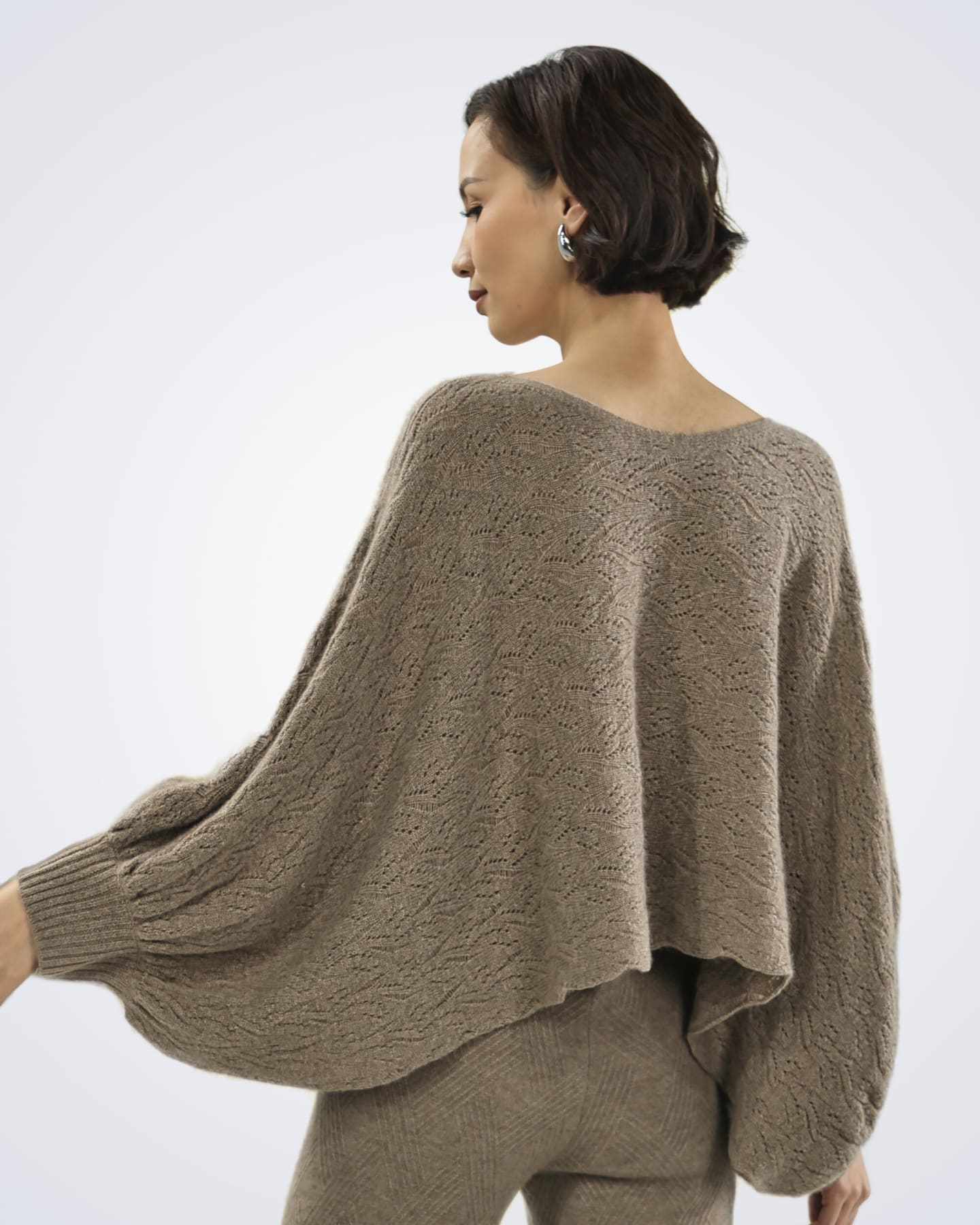 Woman wearing a patterned poncho-style cashmere jumper, rear view
