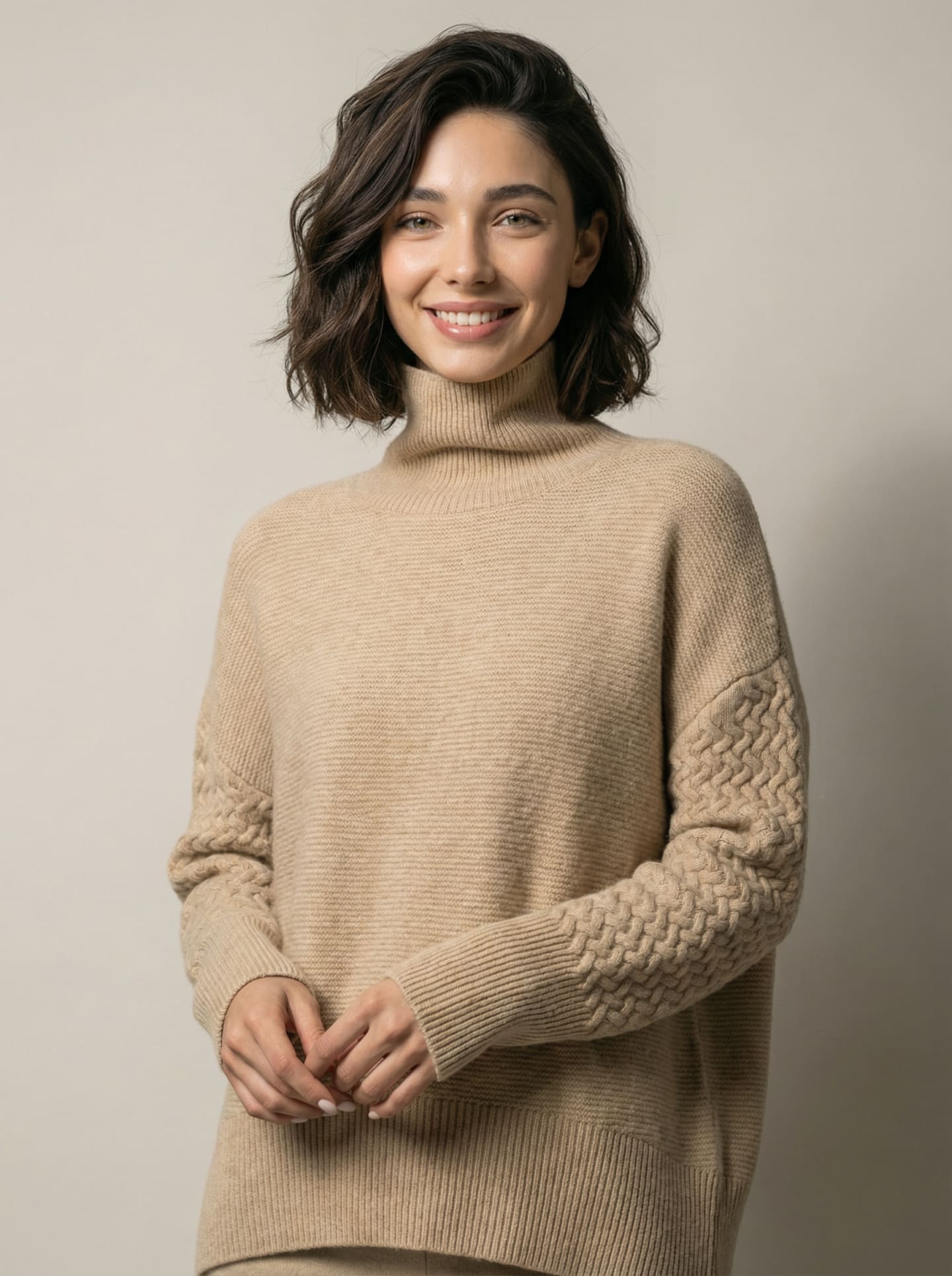Model wearing the oversized cashmere jumper in Natural Beige, front view showing the funnel roll neck, ribbed body and basket-weave cable panel along the sleeves