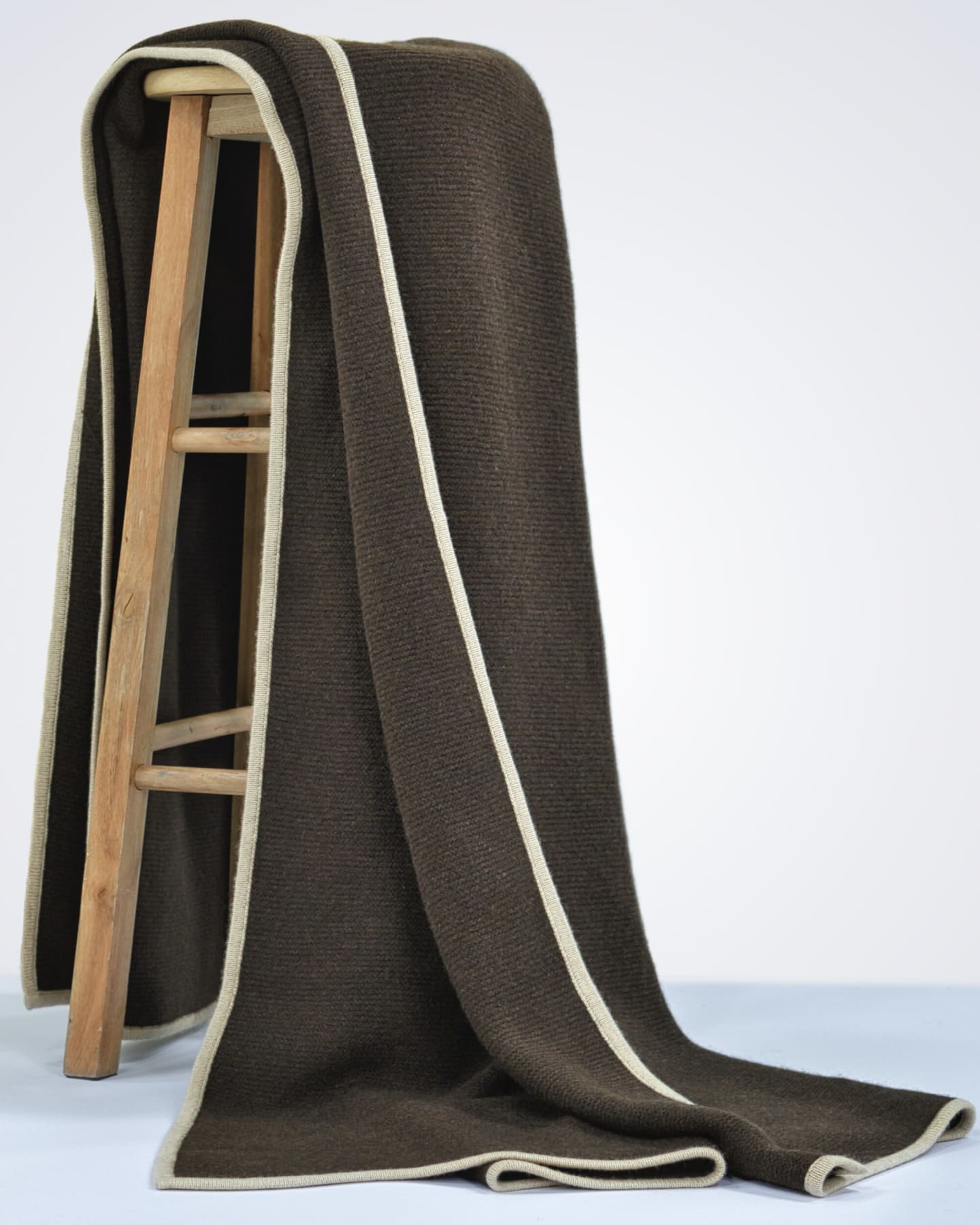Dark chocolate brown knitted yak wool throw with cream border draped full-length over a wooden ladder against a white studio background