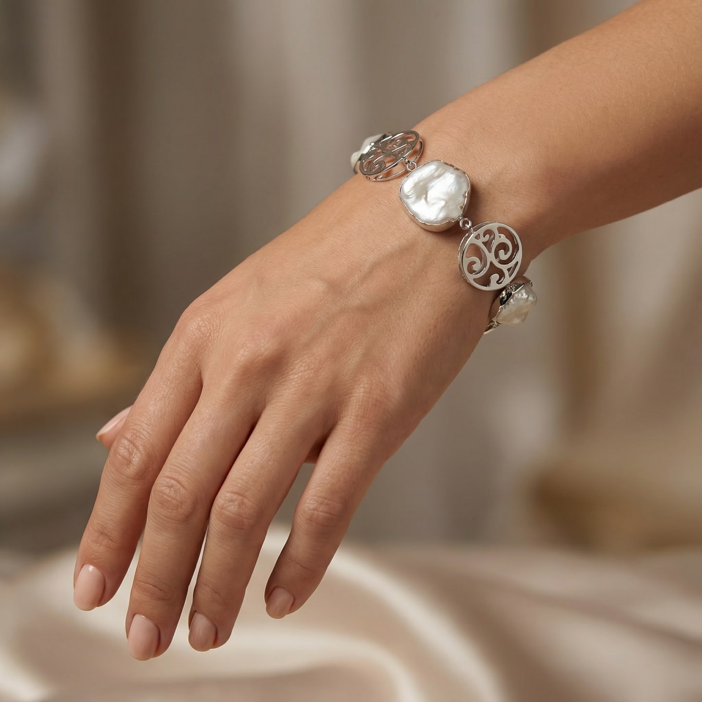 Model wears the Signature Keshi Pearl Statement Chain Bracelet on her wrist; flat keshi freshwater pearls in polished silver bezels alternate with openwork silver scrollwork discs against a soft draped fabric backdrop.