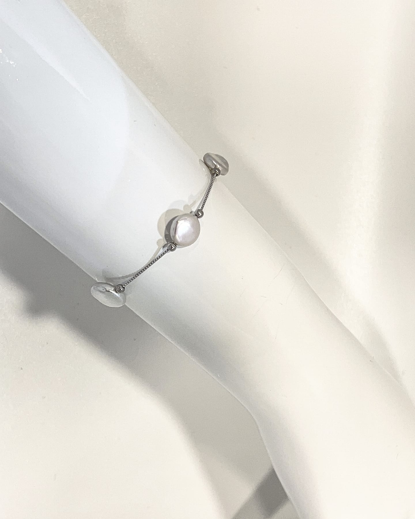 Close-up of the white variant, white dome-fronted button pearls spaced along a fine silver satellite chain with bead spacers