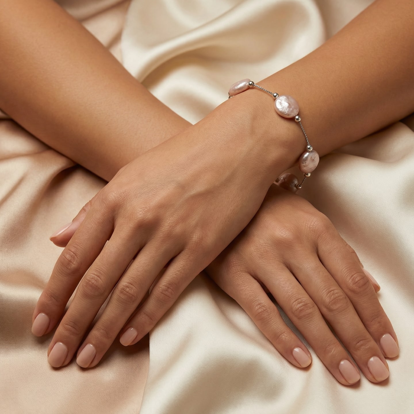 Hand wearing the peach variant of the Classic Button Pearl Satellite Chain Bracelet, flat-disc peach coin pearls on a fine silver chain