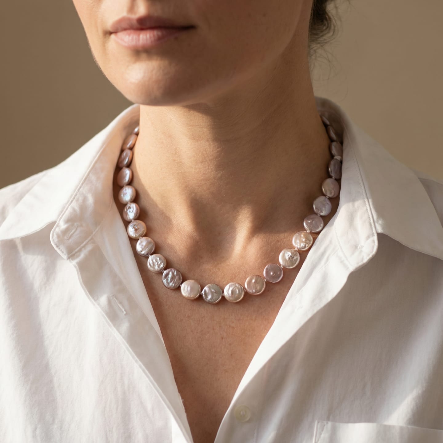 Woman wearing a knotted multi-colour button pearl strand necklace at the collarbone over a white shirt, natural peach and lavender pearl tones