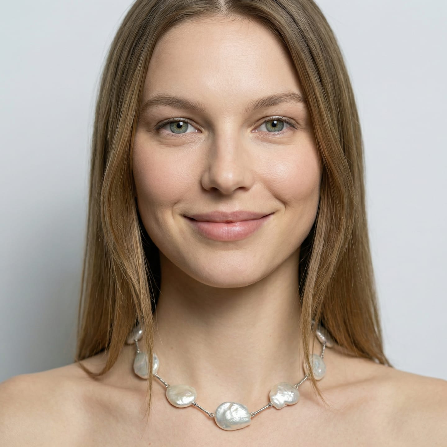 Woman wearing a station necklace at the collarbone, large flat coin freshwater pearls linked by twisted rope-textured silver bar segments