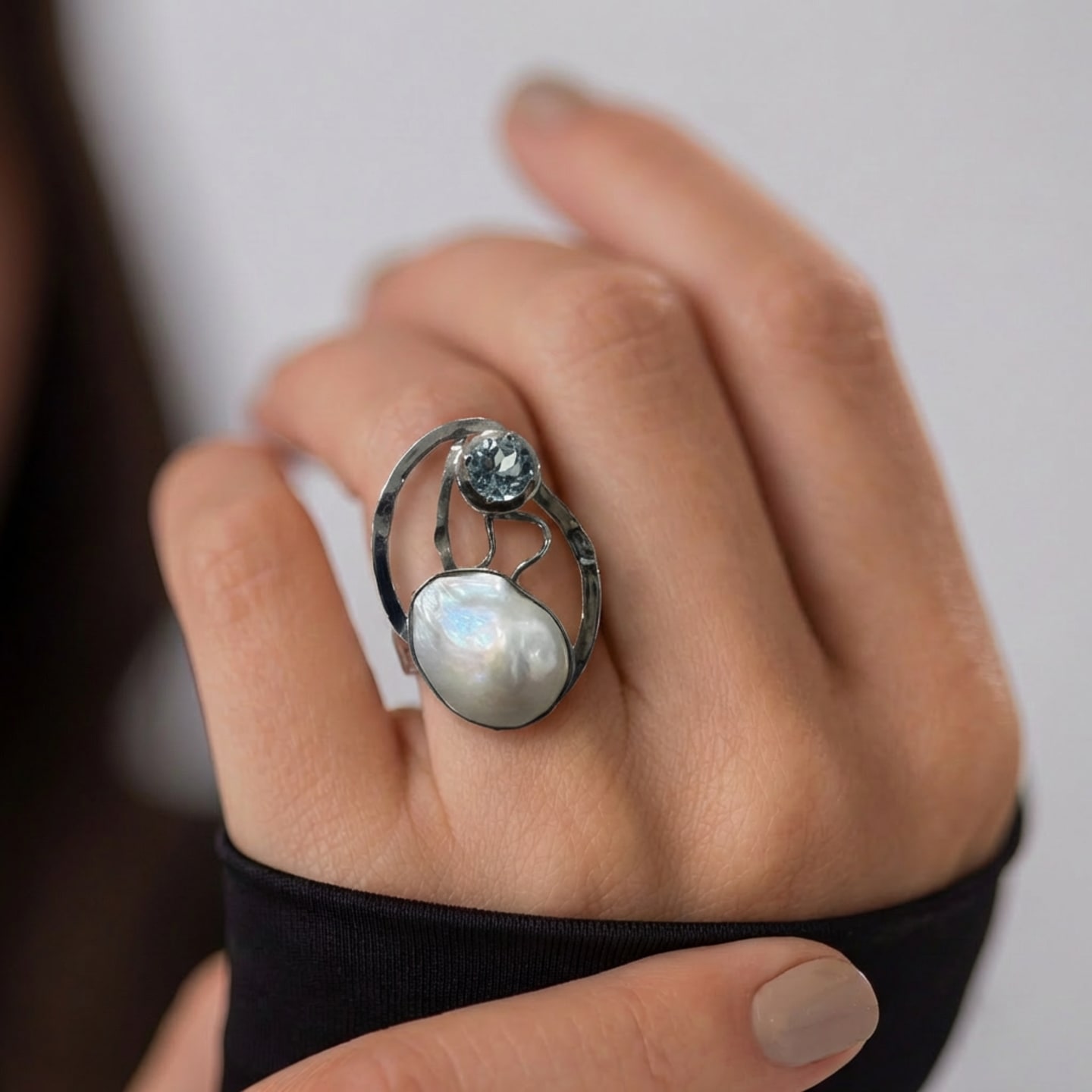 Hand wearing the Signature Baroque Pearl and Topaz Statement Ring in Silver, iridescent coin pearl paired with a faceted blue topaz in an open oval frame