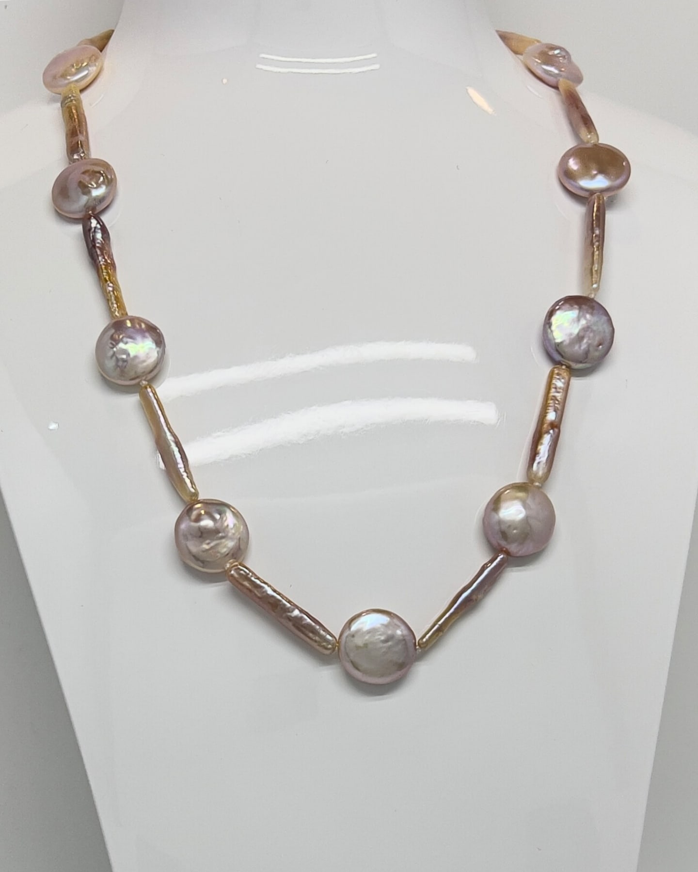Close-up of a pearl strand necklace on a white display bust, alternating coin pearls and biwa pearls in purple-pink with lavender-rose iridescence