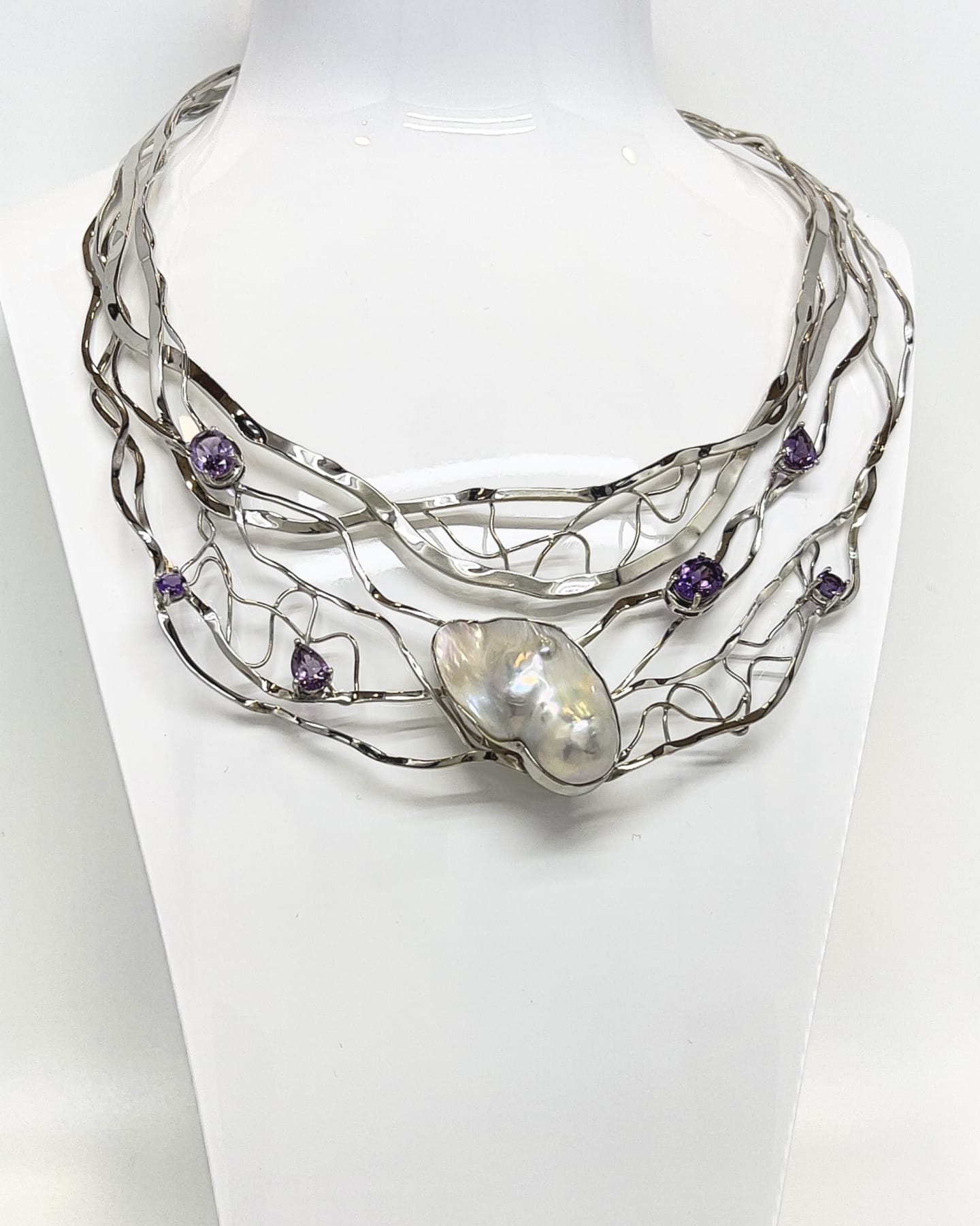 Multi-tier open-back silver torque collar with central baroque pearl and six amethysts, on a white bust display.