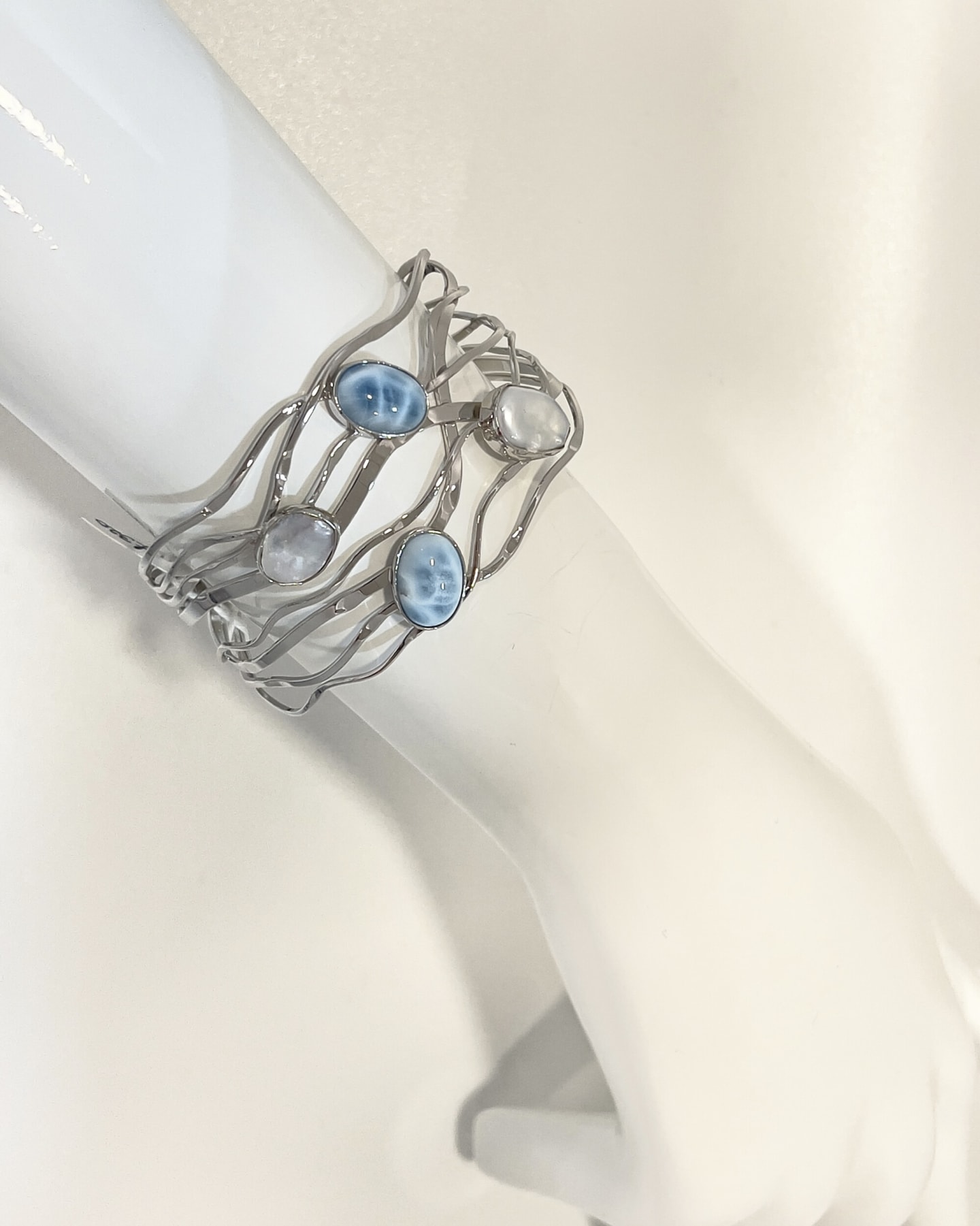 Side-profile view of the Signature open silver wave-form cuff on a white cylindrical display form, two larimar cabochons and two freshwater keshi pearls in oval bezel settings