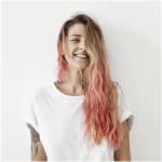 Woman with pink hair smiling in front of white wall