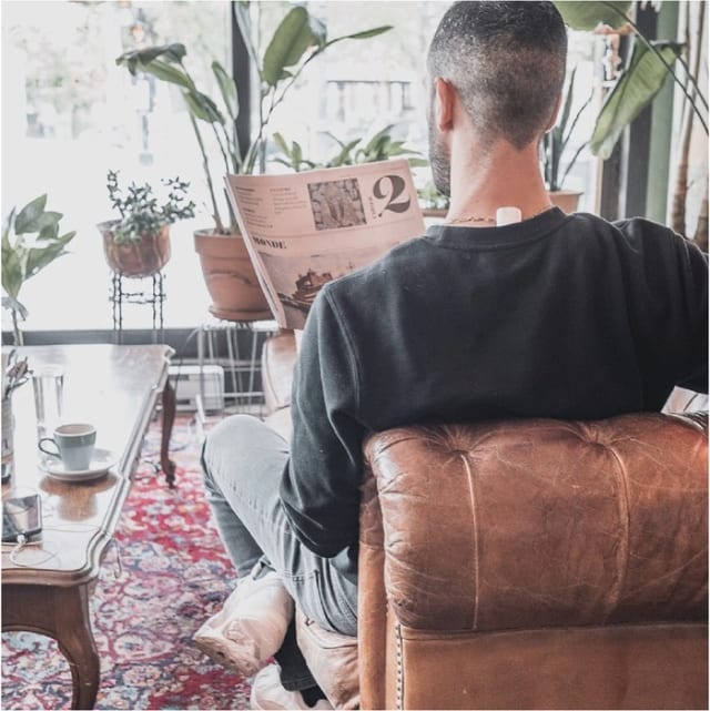 Man with Upright Go on his upper back reading the newspaper on a brown sofa