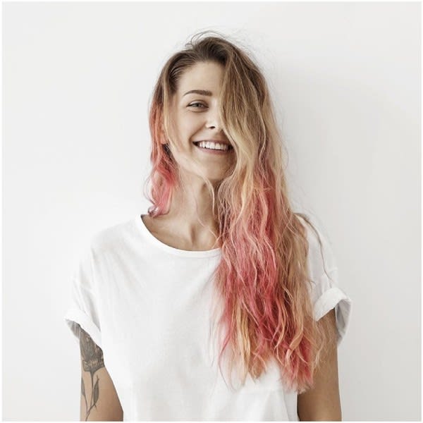 Woman with pink hair smiling in front of white wall