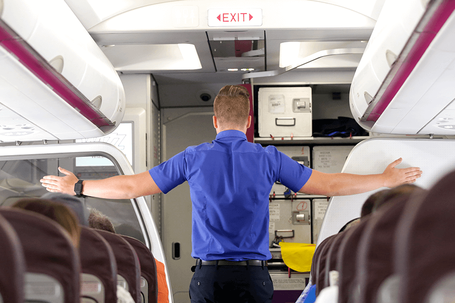 Male flight attendant pointing to emergency exits with both hands.