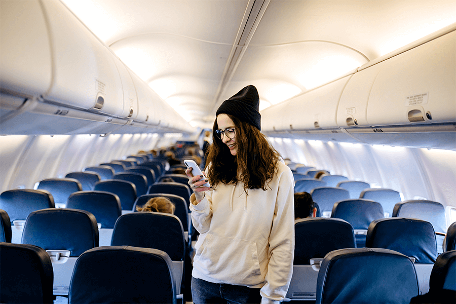 Woman standing in aisle looking at her smartphone, demonstrating poor travel posture.