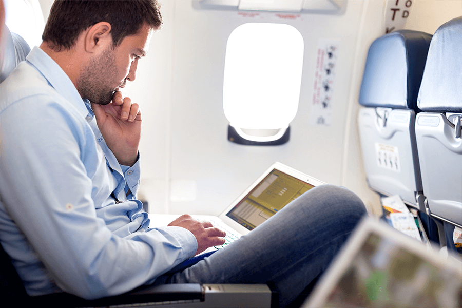 Male passenger looking at a laptop on his lap, demonstrating poor travel posture.