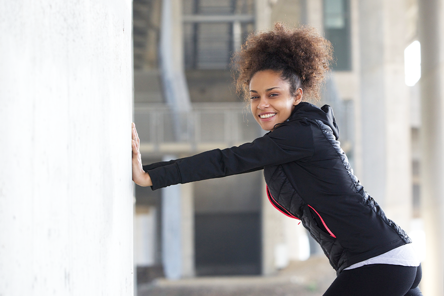 Woman stretching against a wall to prevent rounded shoulders.