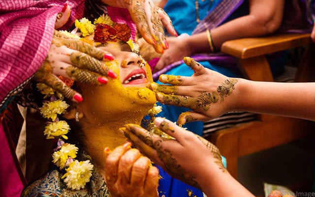 Vibrant Yellow Haldi being put on the bride's face by Flgroe Studios Wedding-photography | Weddings Photos & Ideas