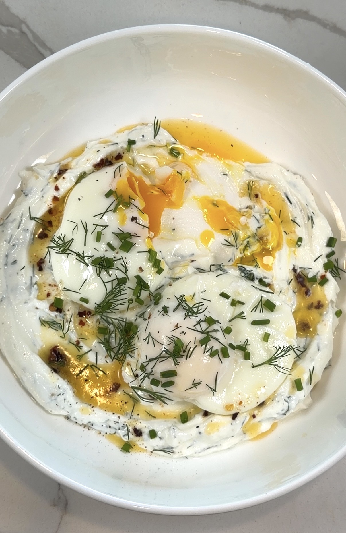 Turkish eggs with poached eggs, garlic dill yogurt, chili butter, dill, and chives