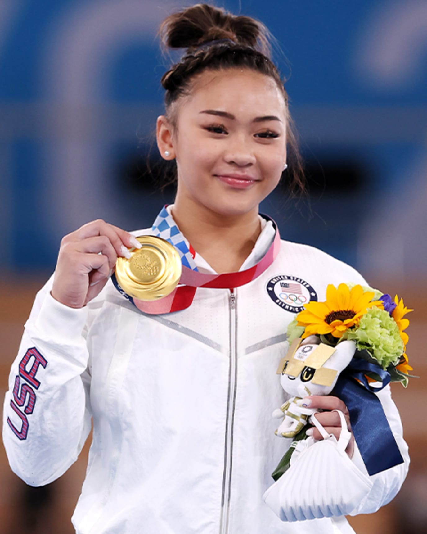 Sunisa Lee holds her gold medal up from the podium