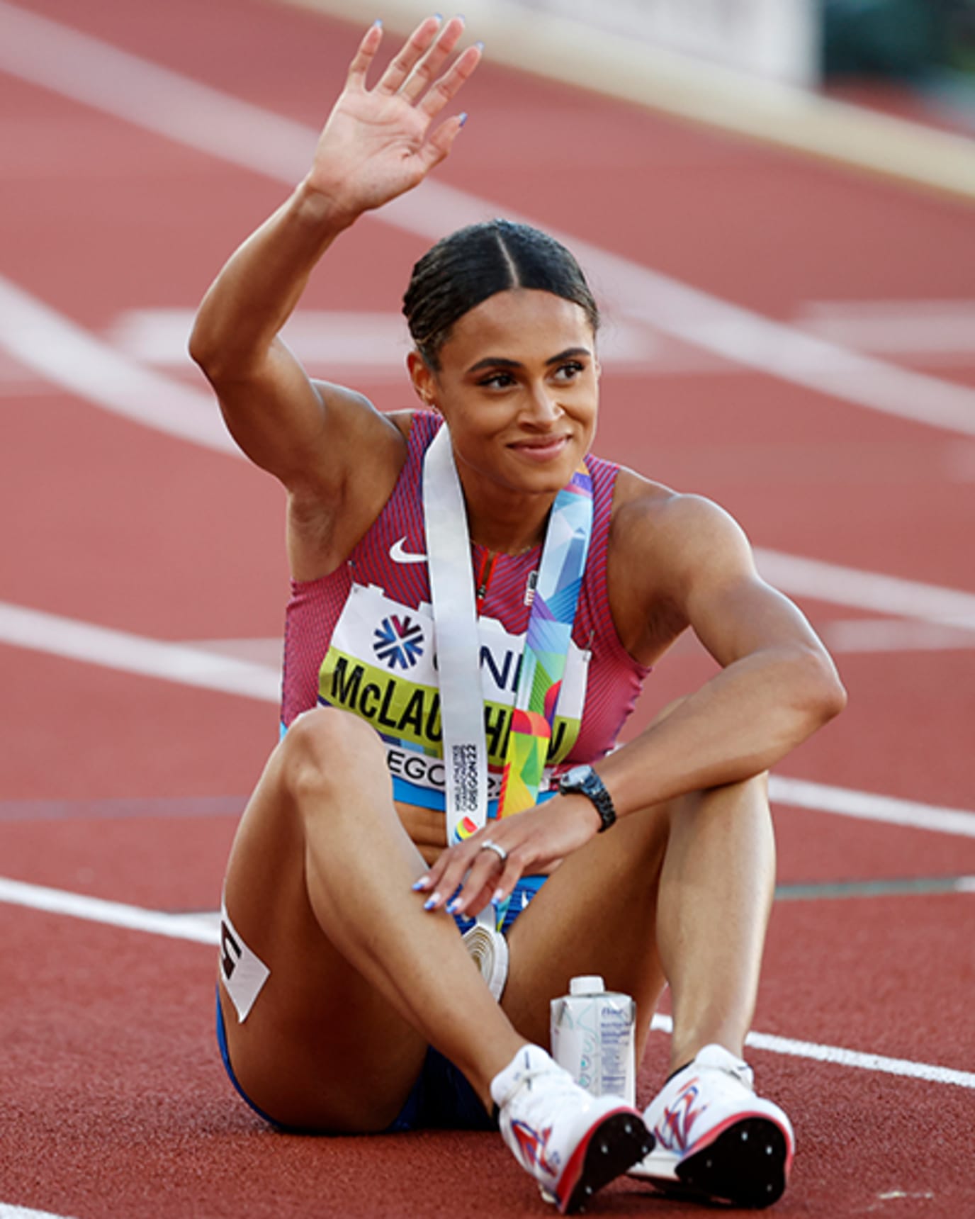 Sydney McLaughlin smiles and waves of the crowd while sitting on the track