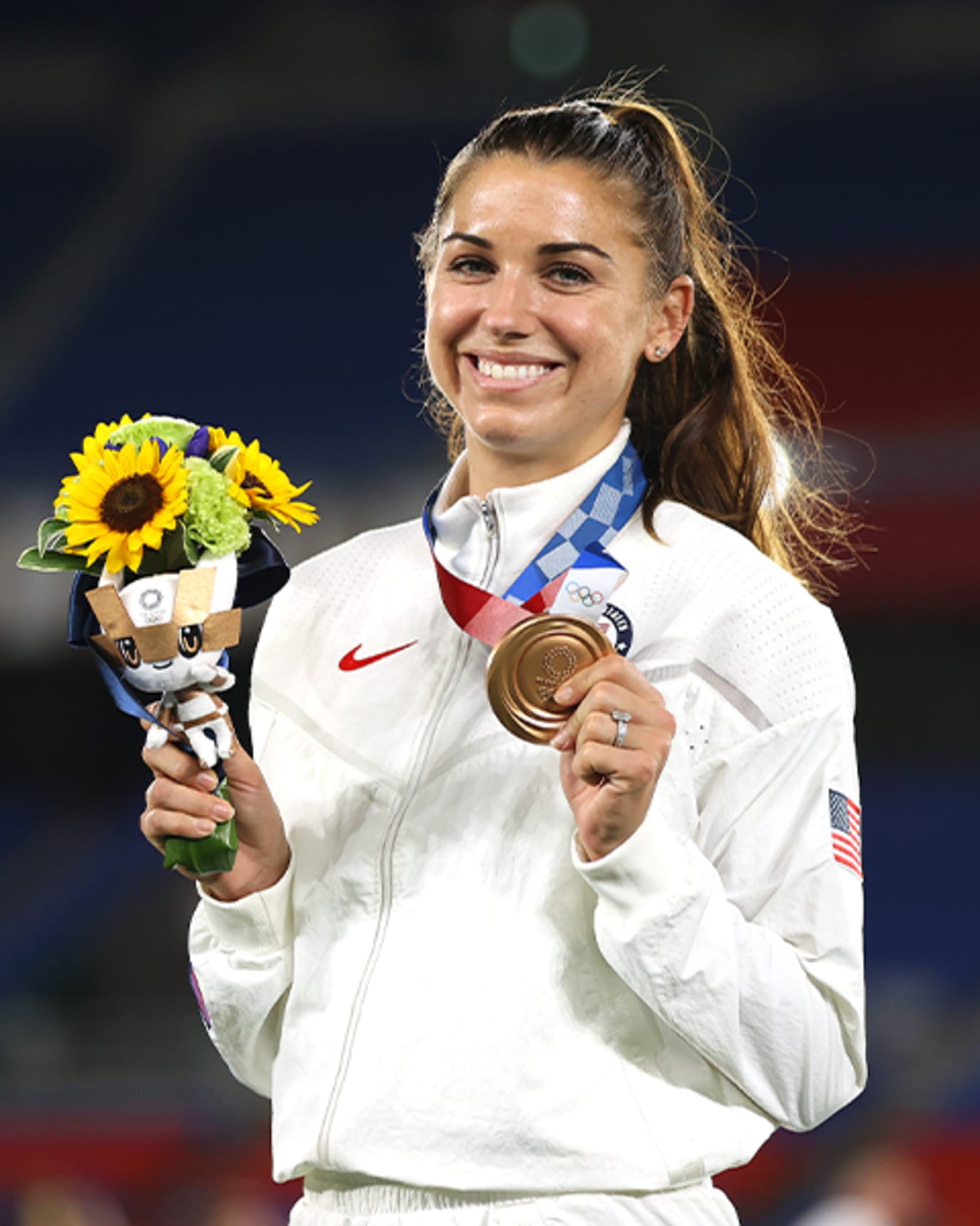 Alex Morgan smiles, and holds up her bronze medal